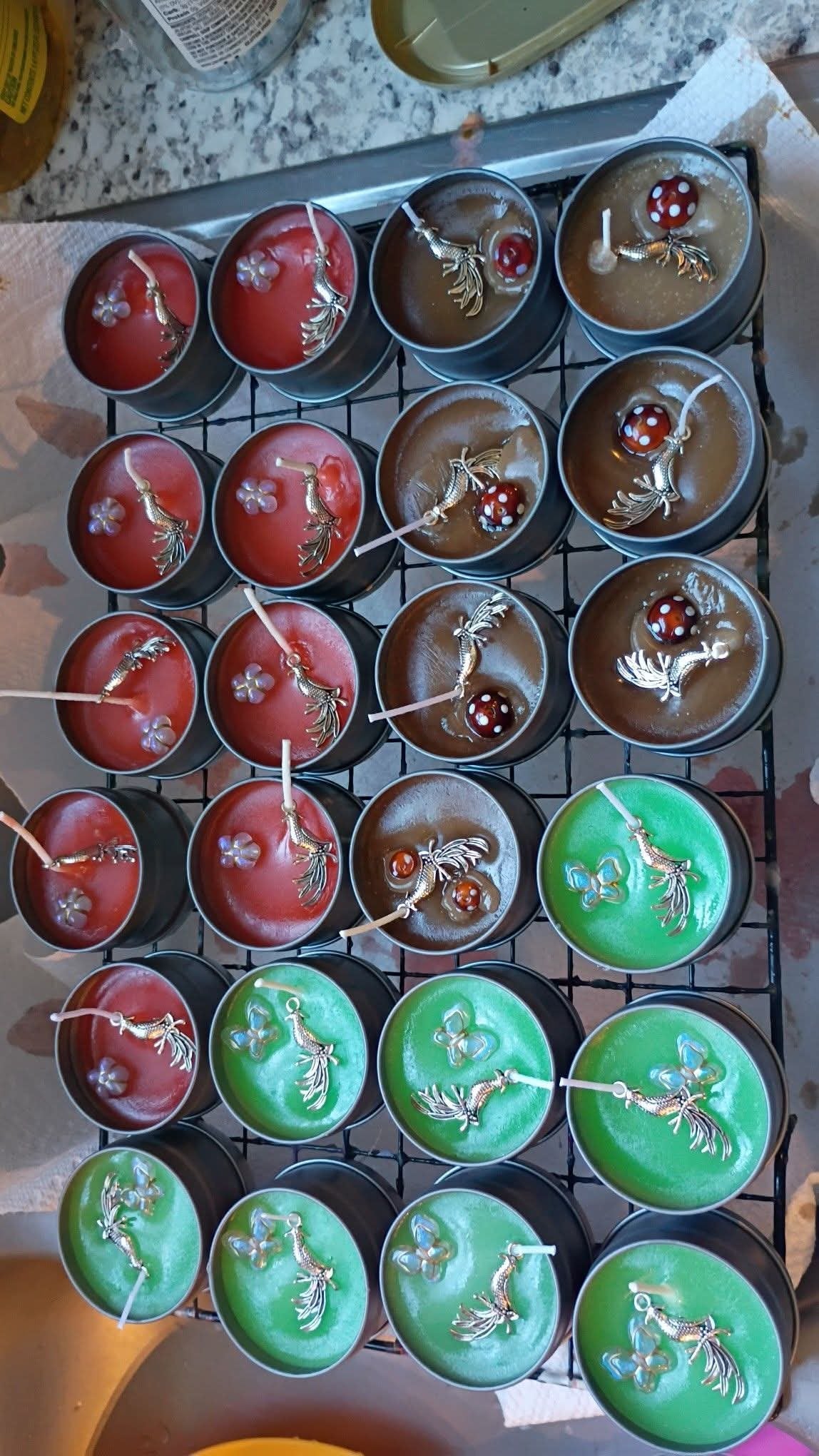 Cooling rack of hand-poured 2 oz scented tin candles in red, green, and brown