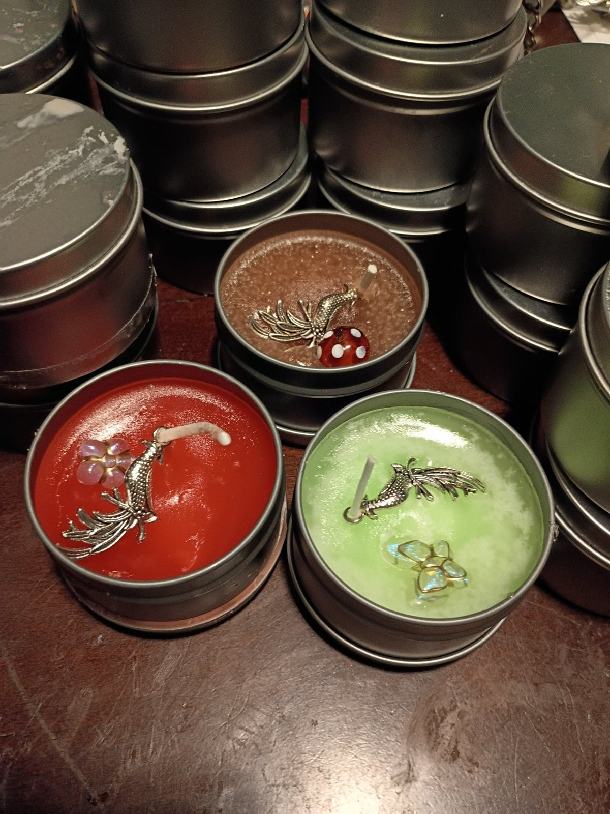 Three 2 oz scented tin candles — red Apple Cinnamon, green Apple, and brown Cinnamon — each topped with a silver phoenix charm