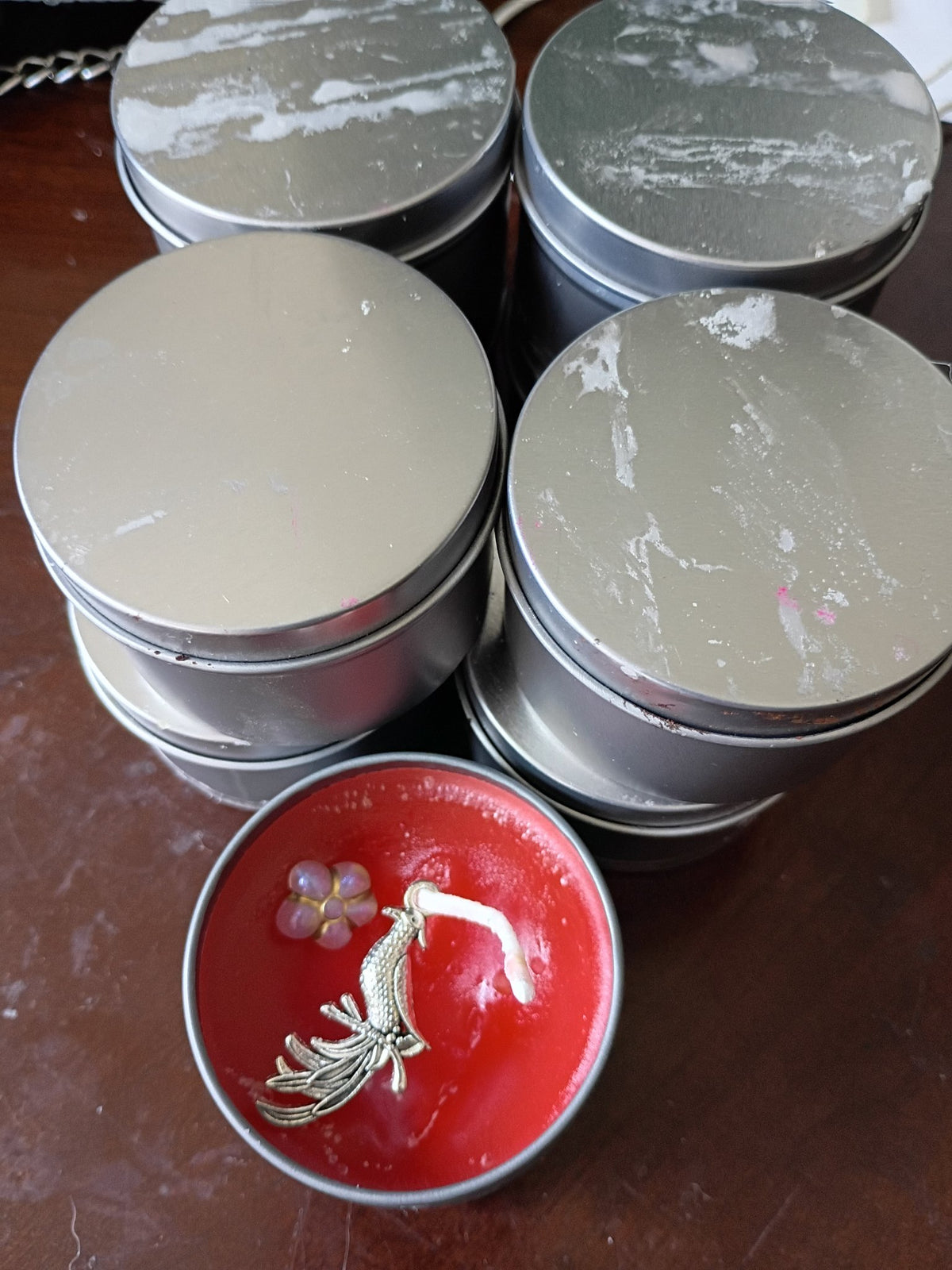 2 oz scented tin candles with lids, red Apple Cinnamon candle open showing phoenix charm and flower bead